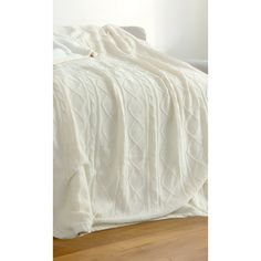 a white blanket on top of a bed next to a wooden floor and a window