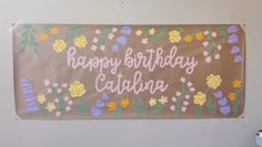 a birthday sign hanging on the side of a wall with flowers and leaves painted on it