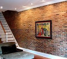 a living room filled with furniture and a brick wall next to a stair case in front of a painting on the wall