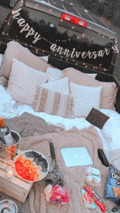 a bed covered in blankets and pillows next to an open trunk with food on it