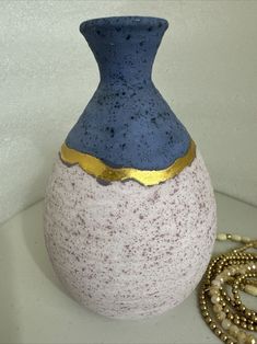 a blue and white vase sitting on top of a table next to a gold necklace