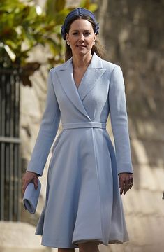 a woman in a blue coat and hat walks down the street