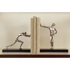 two metal figurines standing next to each other on top of a book shelf