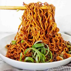 a bowl full of noodles with chopsticks sticking out of the top and green onions in the bottom