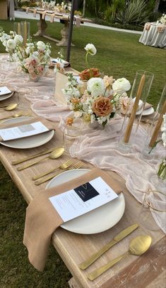 a table set up with place settings and gold utensils for an outdoor wedding reception