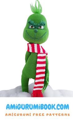 a green stuffed animal wearing a red and white striped scarf on top of snow covered ground