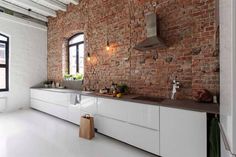 a kitchen with white cabinets and brick wall behind the countertop, along with a large window