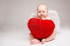 a baby sitting on the ground holding a red heart