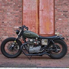 a motorcycle parked in front of a red brick wall with an old door behind it