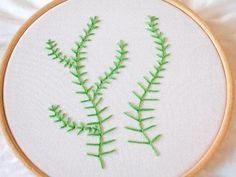 a close up of a embroidery on a white cloth with green leaves in the middle