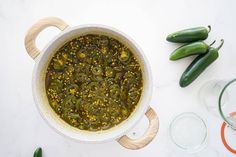 a pot filled with green peppers next to some glasses and spoons on a white surface