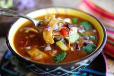 a spoonful of mexican soup is being held by a person's left hand