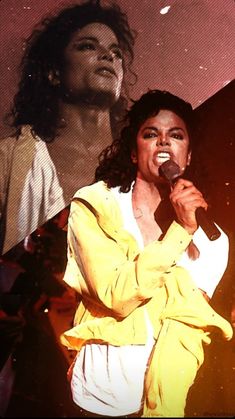 a woman singing into a microphone while standing next to a man with long curly hair