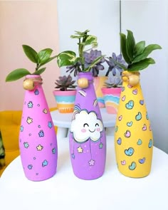 three colorful vases with plants in them sitting on a table next to each other