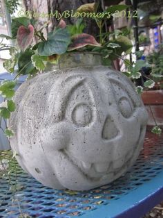 a cement pumpkin planter sitting on top of a blue metal bench with ivy growing in it