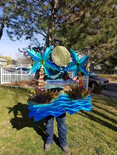 a man standing in the grass holding a blue and green decoration