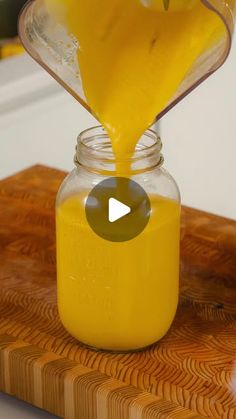 a person pours orange juice into a glass jar on a wooden cutting board,