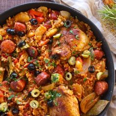 a skillet filled with chicken, rice and olives on top of a wooden table