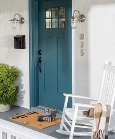 a white rocking chair sitting on top of a porch next to a blue front door