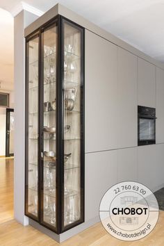 an empty glass cabinet in the middle of a room with hardwood floors and walls, containing dishes and glasses