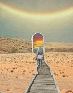 a woman walking down a wooden walkway in the desert with a rainbow painted on it