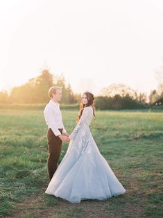 a bride and groom hold hands while standing in a field at sunset with the sun behind them