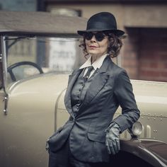 a woman in a suit and hat standing next to an old car