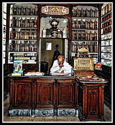 a man sitting at a desk in front of a book shelf filled with books and other items