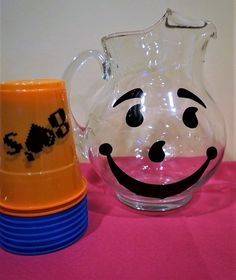 a smiley face glass pitcher next to stack of blue and orange plates