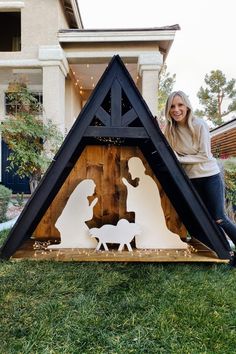 a woman standing next to a nativity scene in front of a house with string lights