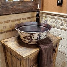 a large metal bowl sitting on top of a wooden cabinet next to a sink and mirror