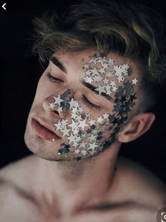 a shirtless man with his face covered in silver and black stars, looking at the camera