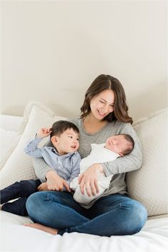 a woman sitting on top of a bed holding a baby and smiling at the camera