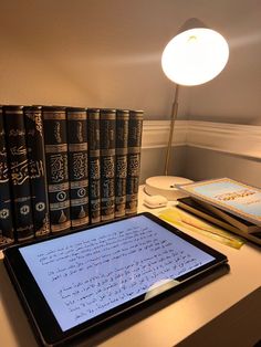 a tablet sitting on top of a desk next to stacks of books and a lamp