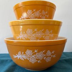 three yellow bowls sitting on top of a blue cloth covered tablecloth with flowers painted on them