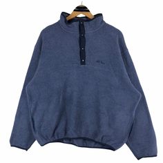 a blue sweatshirt that is hanging on a wooden hanger with a black button down the middle