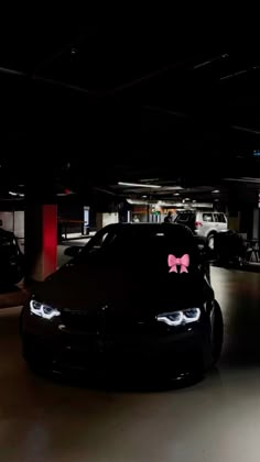 two cars parked in a parking garage with pink bows on the hood