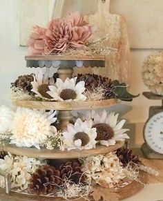 three tiered cake with flowers and pine cones on the top, next to an alarm clock