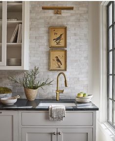 a kitchen with white brick walls and black counter tops, two framed pictures above the sink