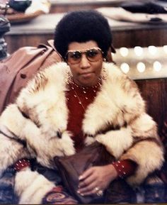 an old photo of a woman sitting on a couch wearing sunglasses and a fur coat