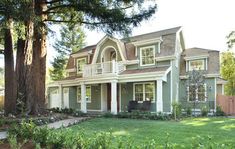 a large house sitting next to a tree in front of a lush green yard with lots of trees