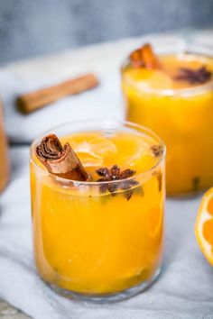 two glasses filled with orange juice and cinnamon sticks