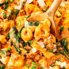 a wooden spoon is in a pasta dish with spinach and other toppings on the side