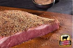 a piece of meat sitting on top of a wooden cutting board next to a bowl of seasoning