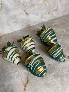 four green and white strawberries sitting on a marble counter top with gold trimmings