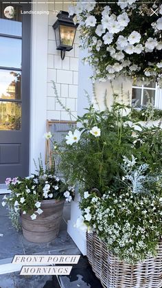 two baskets filled with white flowers sitting on the front porch next to a gray door