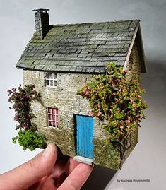 a miniature house made out of clay with flowers growing on the roof and door, in someone's hand