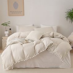 a bed with white sheets and pillows in a room next to a potted plant