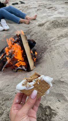 someone is holding up a piece of food in front of a campfire on the beach