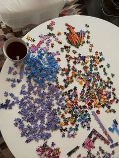 a white plate topped with lots of colorful puzzle pieces next to a cup of coffee